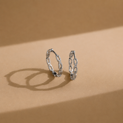 Pair of silver chain-link hoop earrings on a beige background