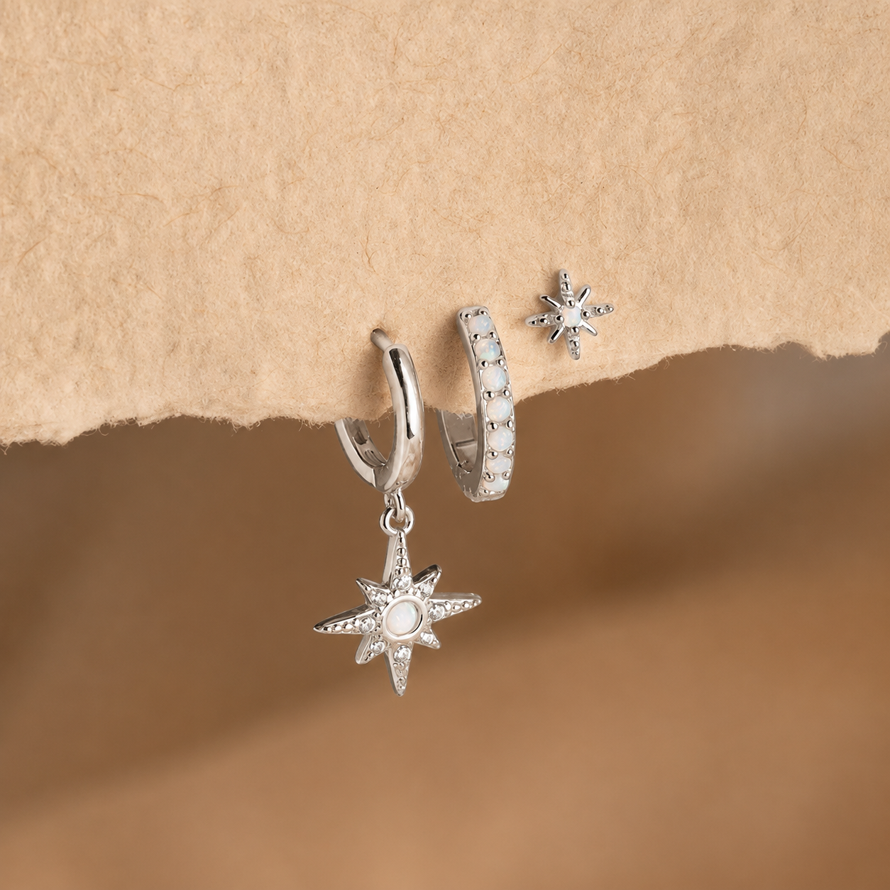 Silver star-shaped earrings on a textured beige background