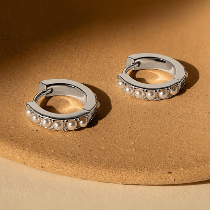 Silver hoop earrings with pearl accents on a beige surface