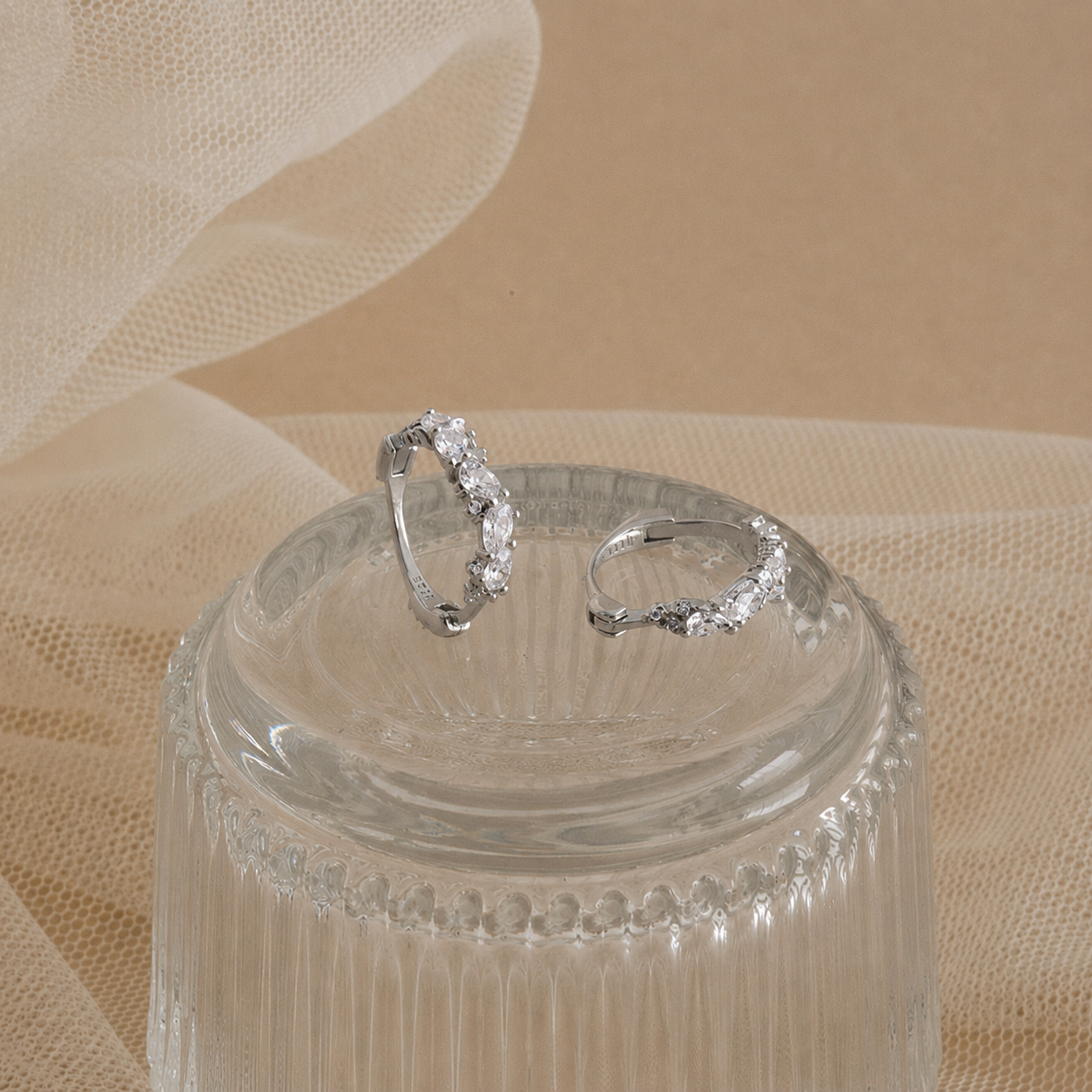 Silver hoop earrings on a clear glass stand with a beige fabric background