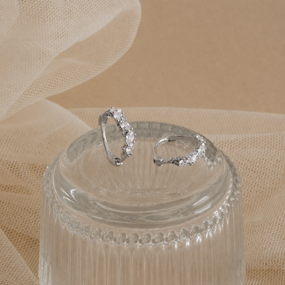 Silver hoop earrings on a clear glass stand with a beige fabric background