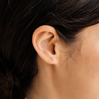 Close-up of an ear wearing a small stud earring with dark hair.
