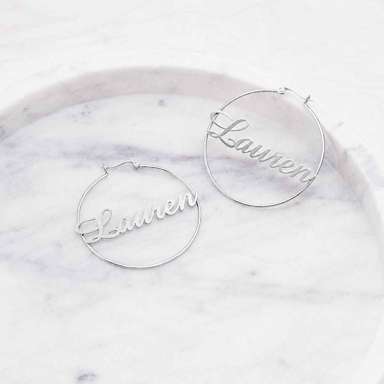 Silver hoop earrings with 'Lauren' engraving on a marble surface