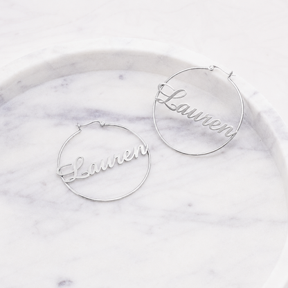 Silver hoop earrings with 'Lauren' engraving on a marble surface
