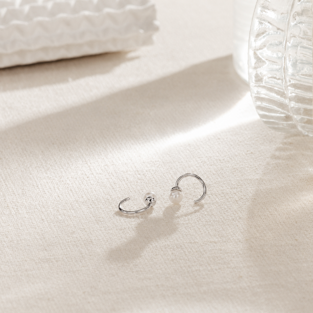 Silver hoop earrings with a pearl on a white surface
