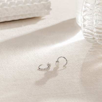 Silver hoop earrings with a pearl on a white surface