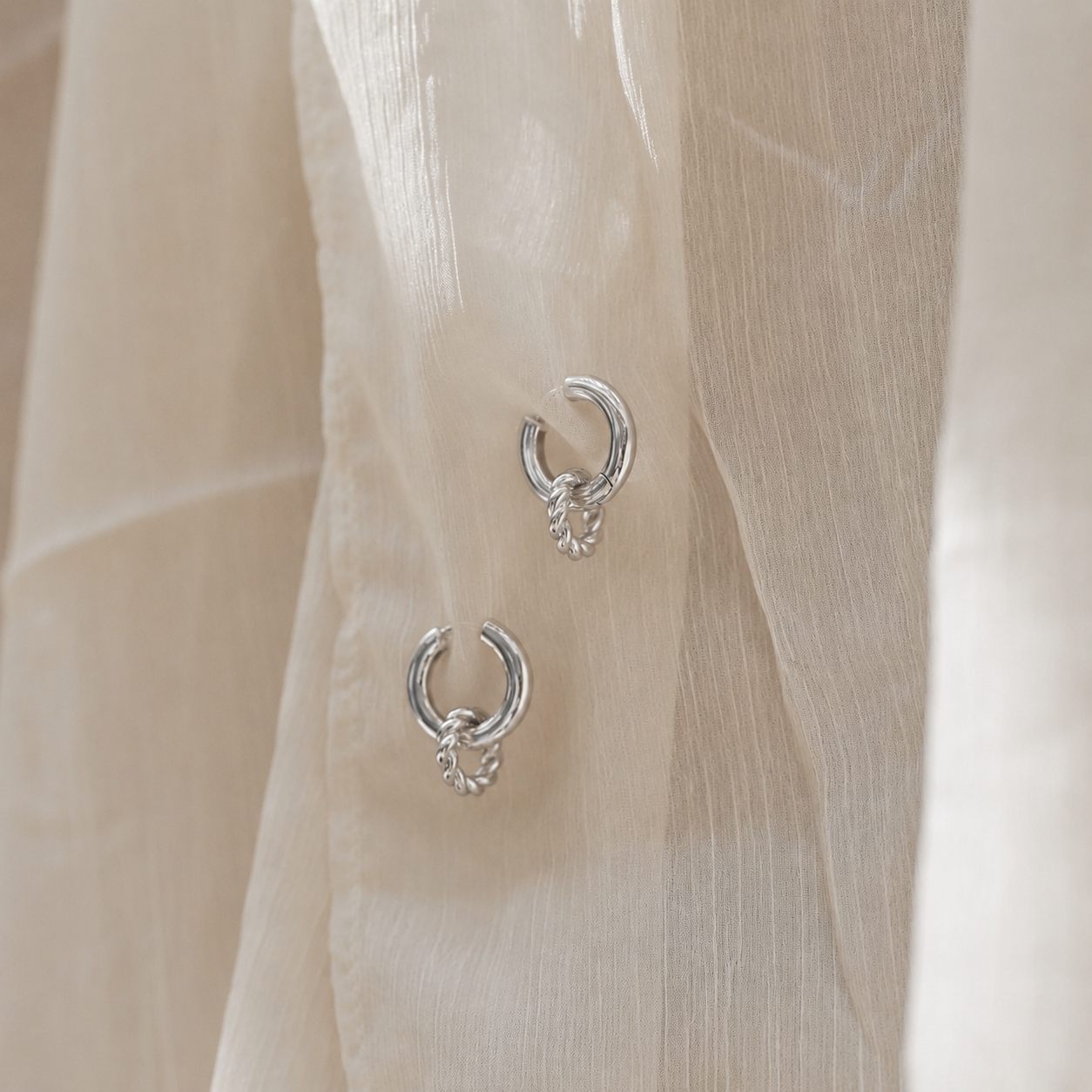 Silver hoop earrings on a sheer beige fabric background