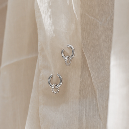 Silver hoop earrings on a sheer beige fabric background