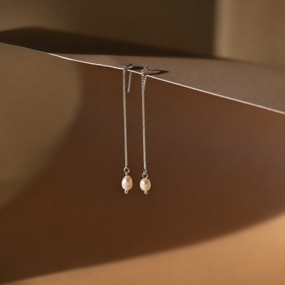 Pair of pearl earrings hanging on a brown surface with soft shadows