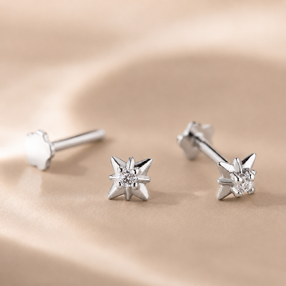 Star-shaped silver earrings with clear gemstones on a beige background
