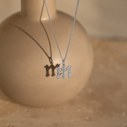 Silver necklace with 'M' pendant on a beige background