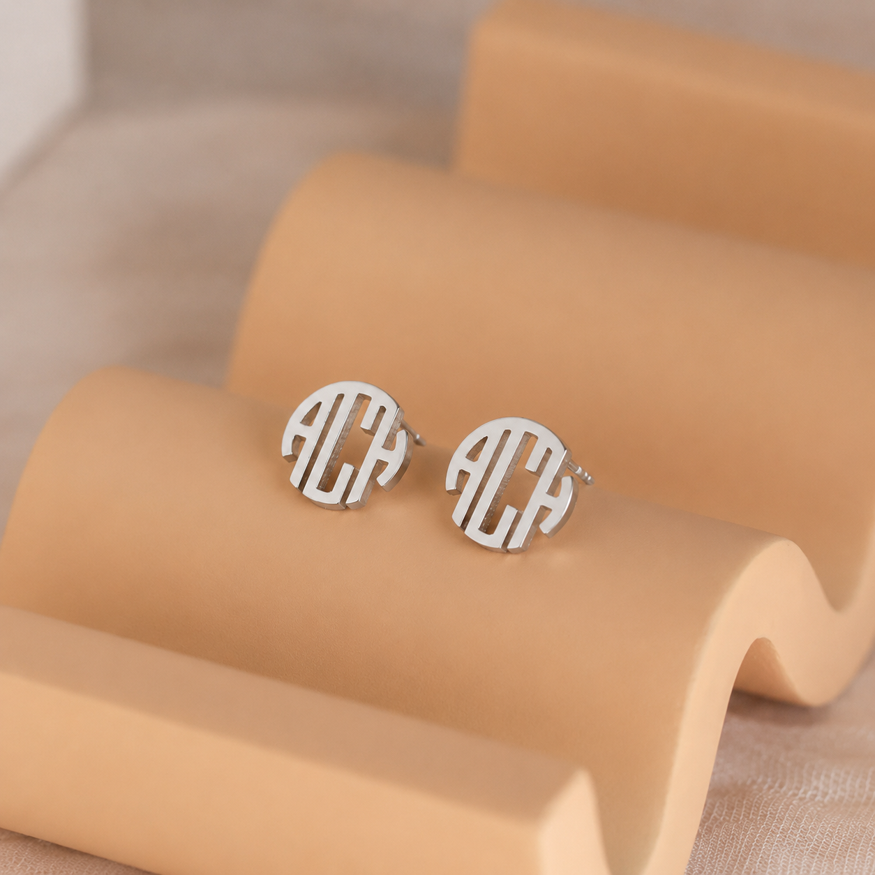 Silver monogram earrings on a beige stand