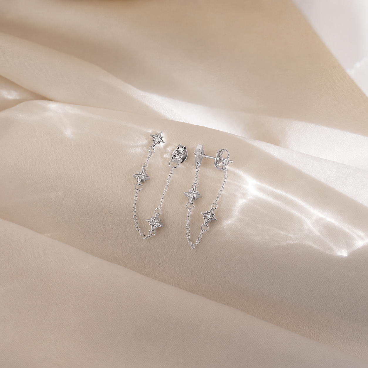 Silver star-shaped earrings on a soft beige fabric background