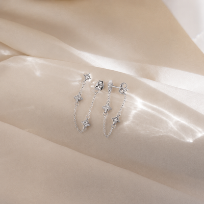Silver star-shaped earrings on a soft beige fabric background