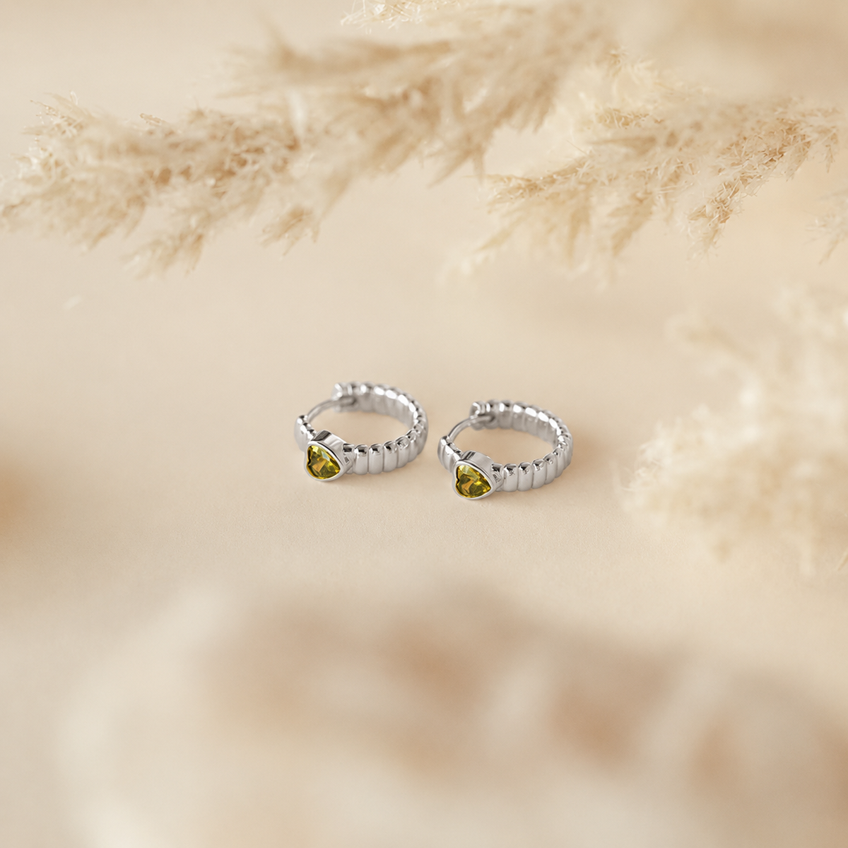 Silver hoop earrings with green gemstones on a beige textured background