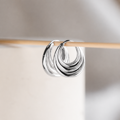 Silver hoop earrings on a wooden stick against a neutral background