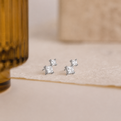 Silver stud earrings with clear gemstones on a beige surface