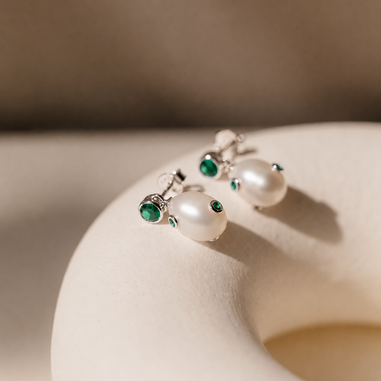 Pearl earrings with green gemstones on a beige surface