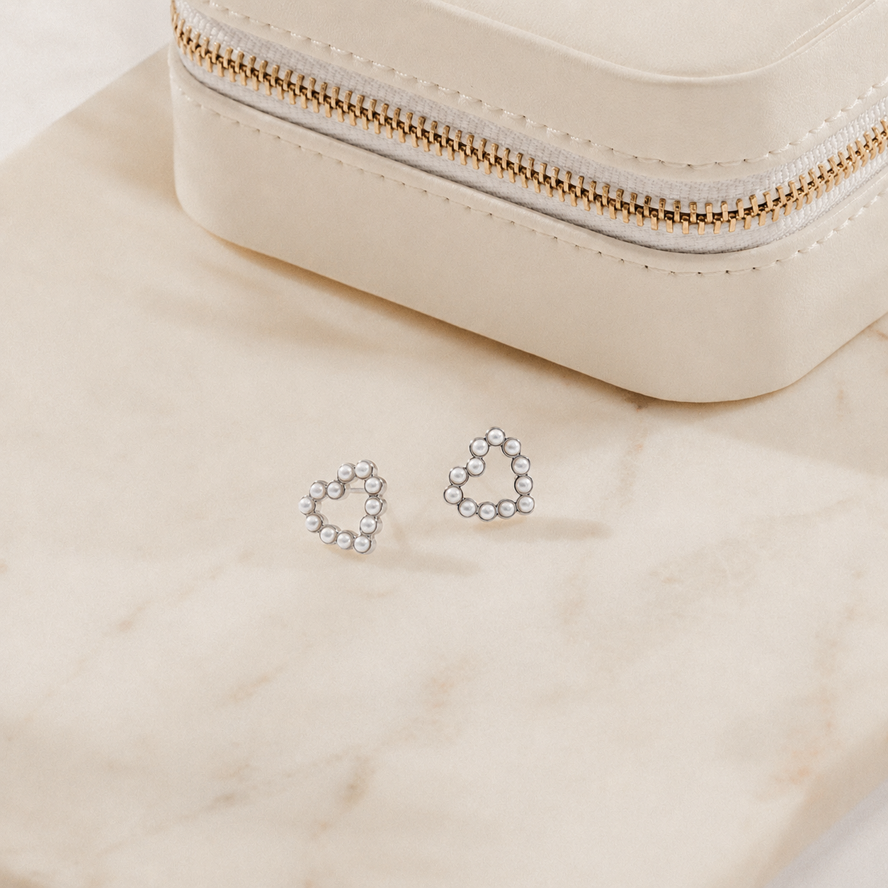 Pearl heart-shaped earrings on a beige surface with a small jewelry box.