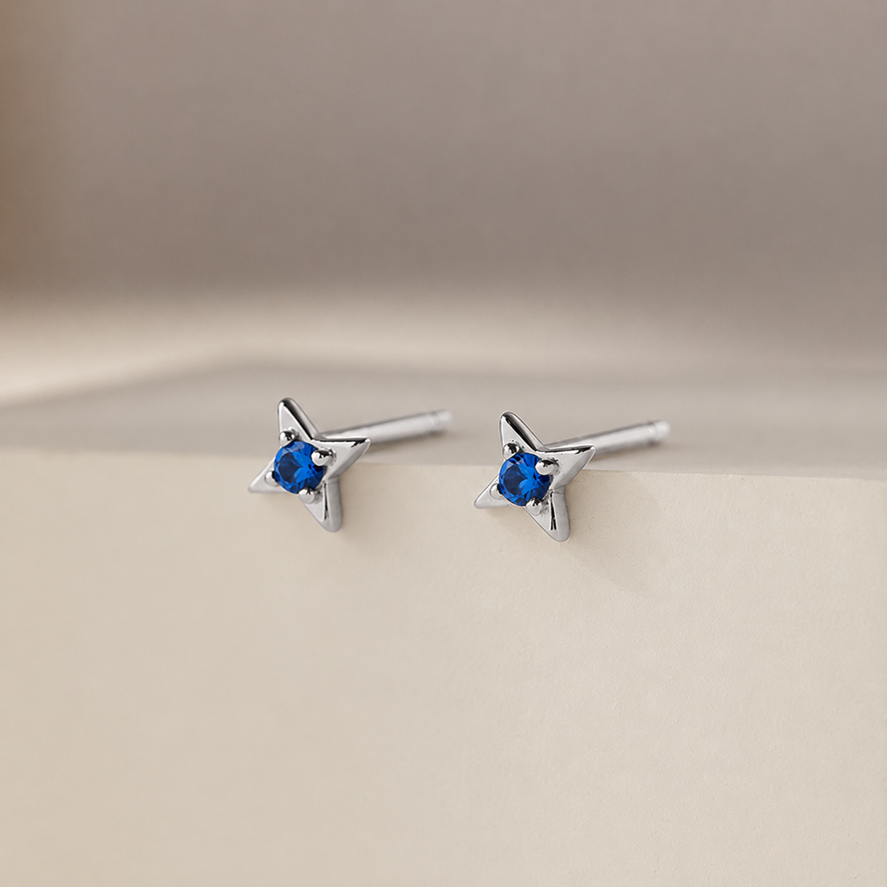 Star-shaped silver earrings with blue gemstones on a beige background