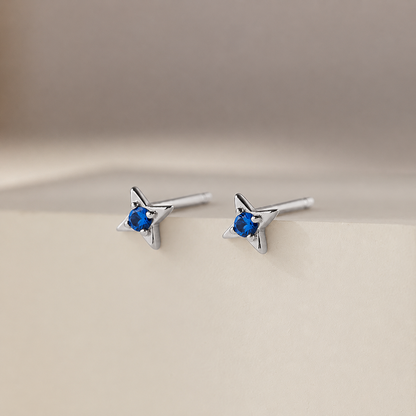 Star-shaped silver earrings with blue gemstones on a beige background