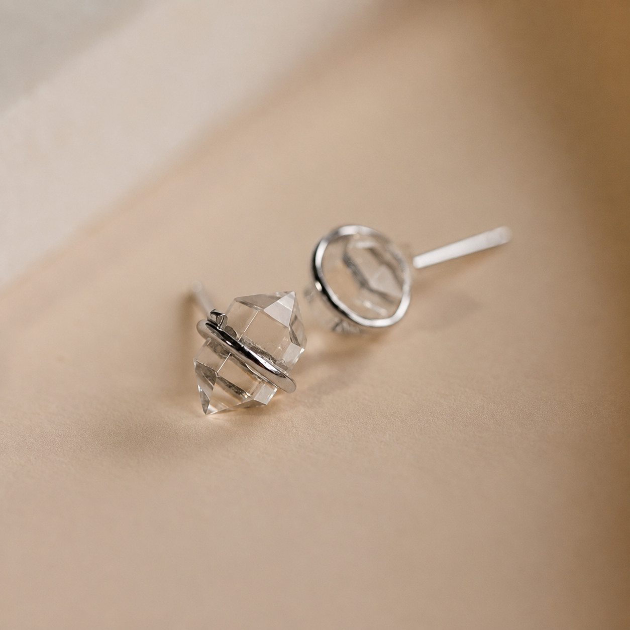 Silver earrings with clear crystal elements on a beige background