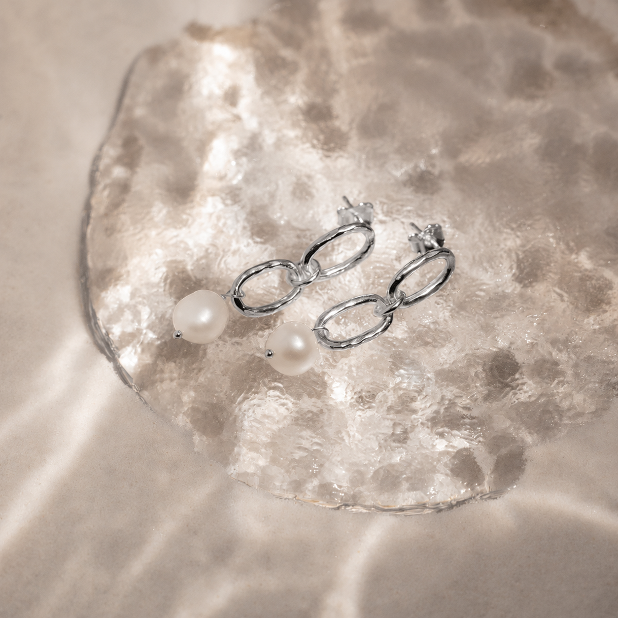 Silver chain earrings with pearls on a textured beige surface