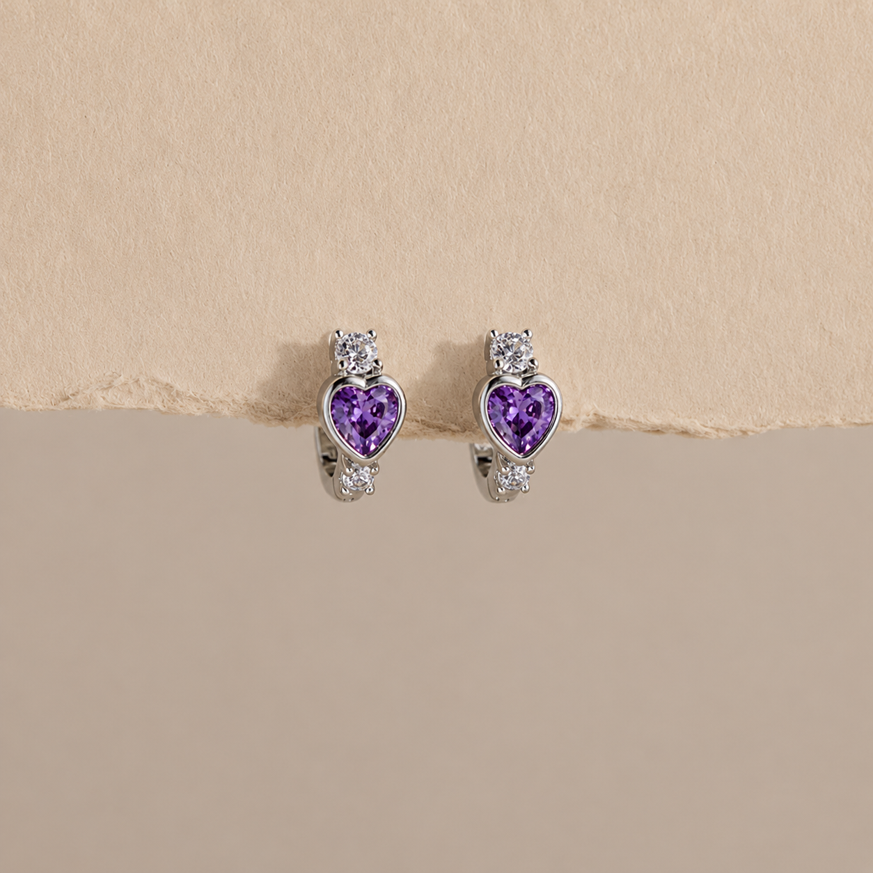 Heart-shaped purple gemstone earrings on a beige background