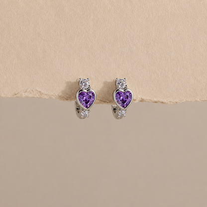 Heart-shaped purple gemstone earrings on a beige background
