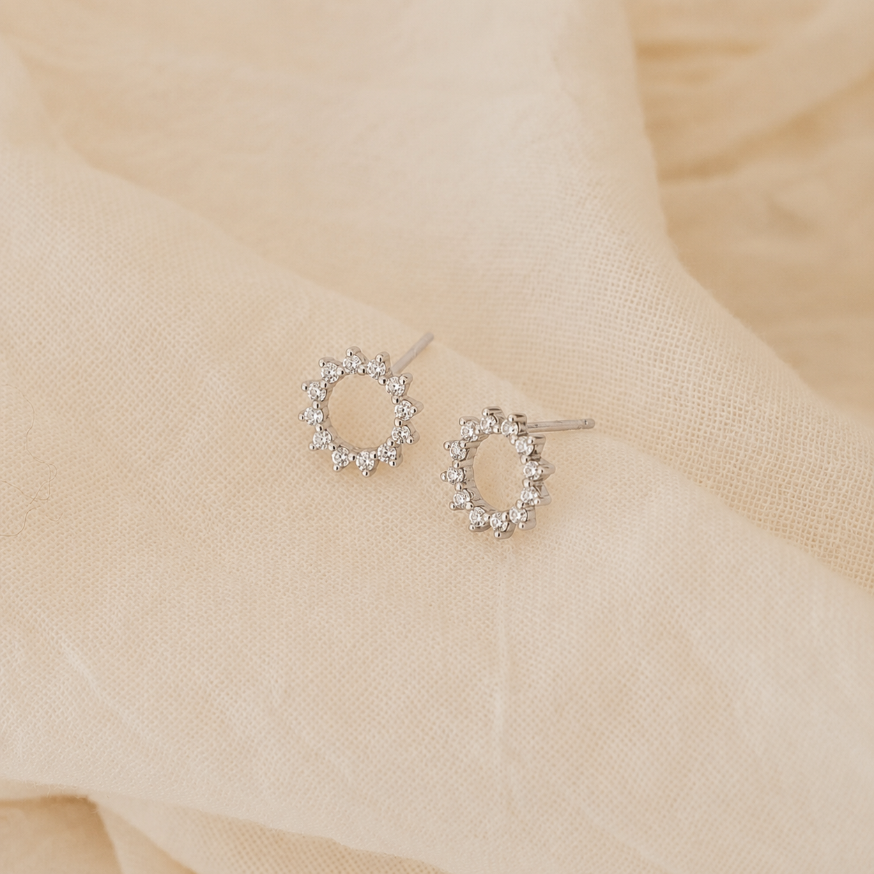 Silver hoop earrings with clear stones on a beige fabric background