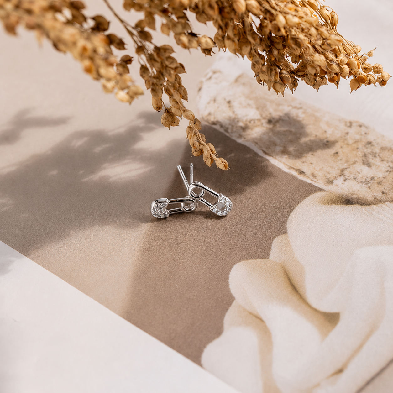 Silver earrings on a neutral background with dried flowers and a white flower.