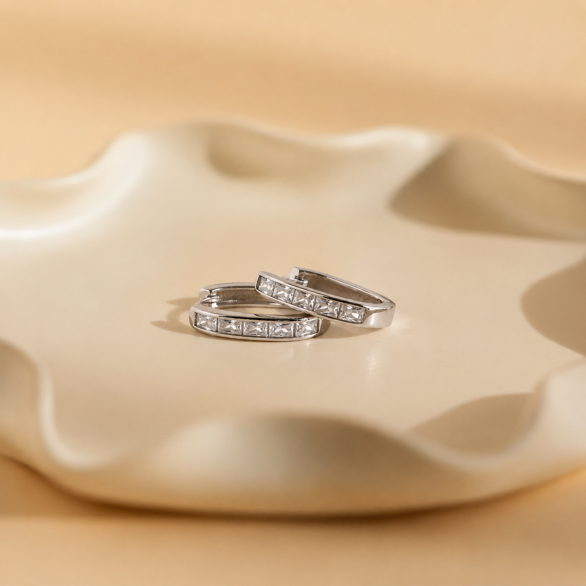 Pair of silver hoop earrings with embedded stones on a beige ceramic dish.