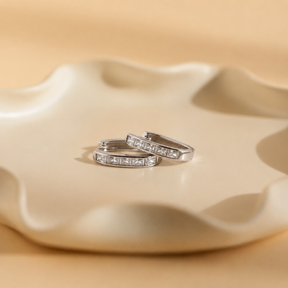 Pair of silver hoop earrings with embedded stones on a beige ceramic dish.