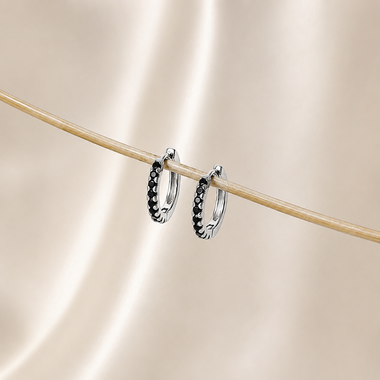 Silver hoop earrings with black stones on a beige background