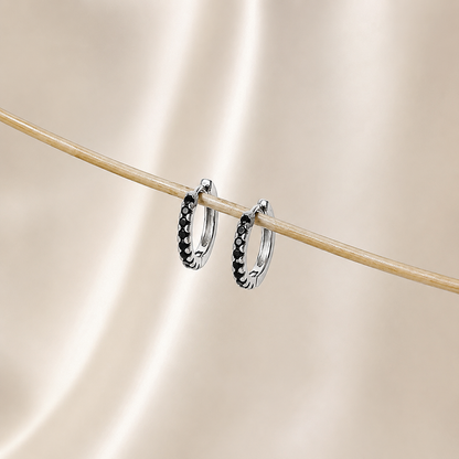 Silver hoop earrings with black stones on a beige background