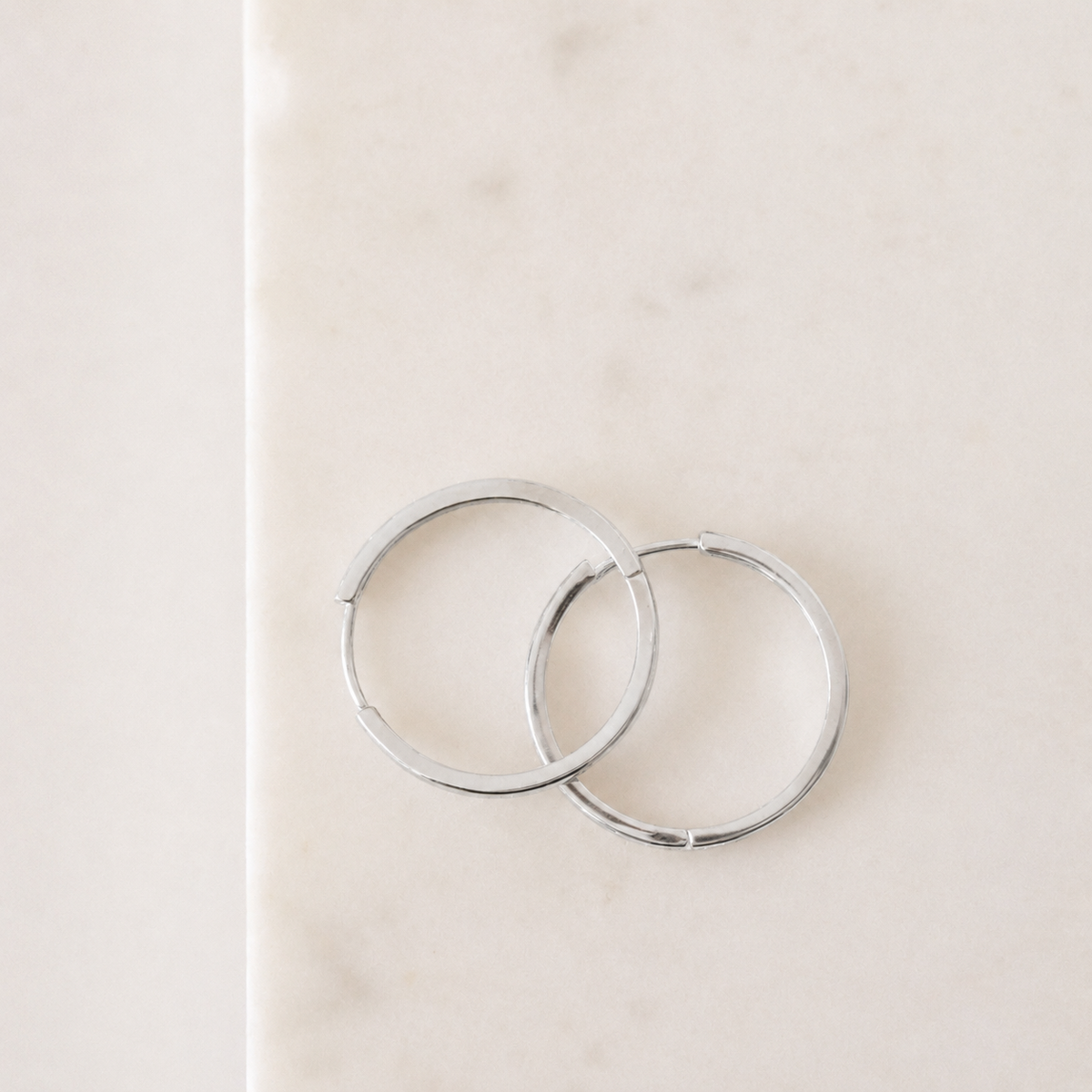 Two silver hoop earrings on a light beige background