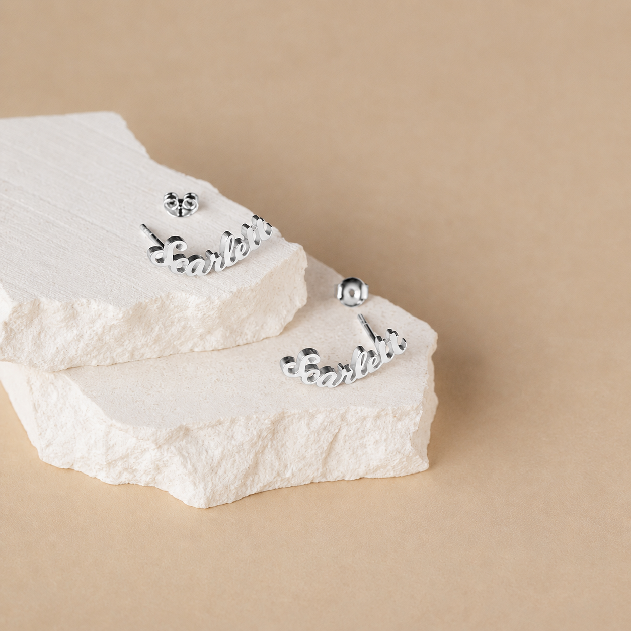 Silver earrings on a textured white box against a beige background