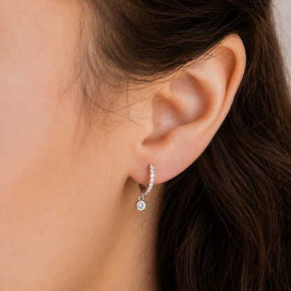 Close-up of an ear wearing a silver hoop earring with a small round pendant.