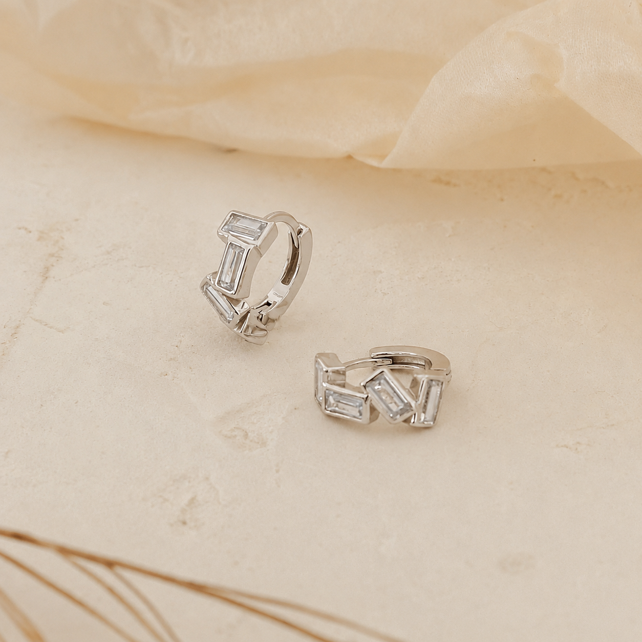 Silver hoop earrings with baguette cut stones on a beige fabric background
