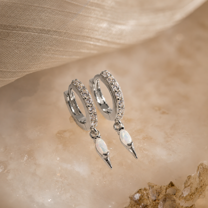 Silver hoop earrings with pearl-like drops on a beige fabric background