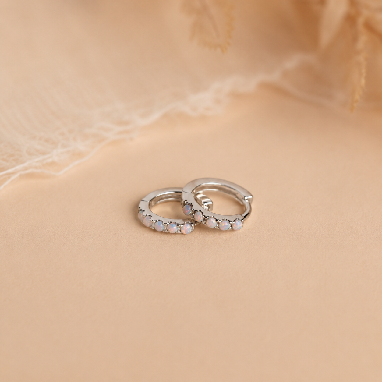 Pair of silver hoop earrings with embedded stones on a beige fabric background