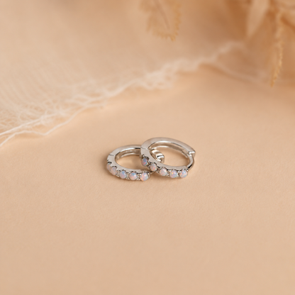 Pair of silver hoop earrings with embedded stones on a beige fabric background