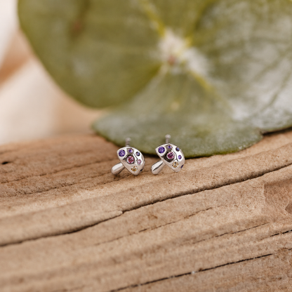 Silver earrings with gemstones on a wooden surface with a leaf in the background