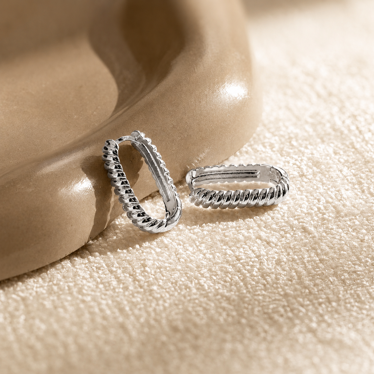 Silver hoop earrings on a beige surface