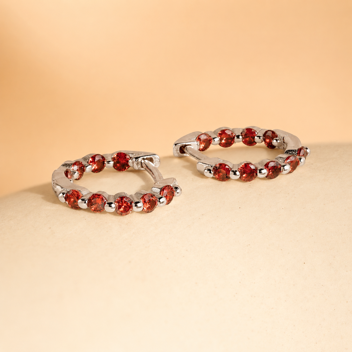 Silver hoop earrings with red gemstones on a beige surface