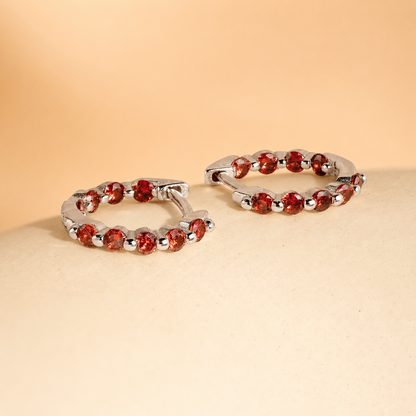 Silver hoop earrings with red gemstones on a beige surface