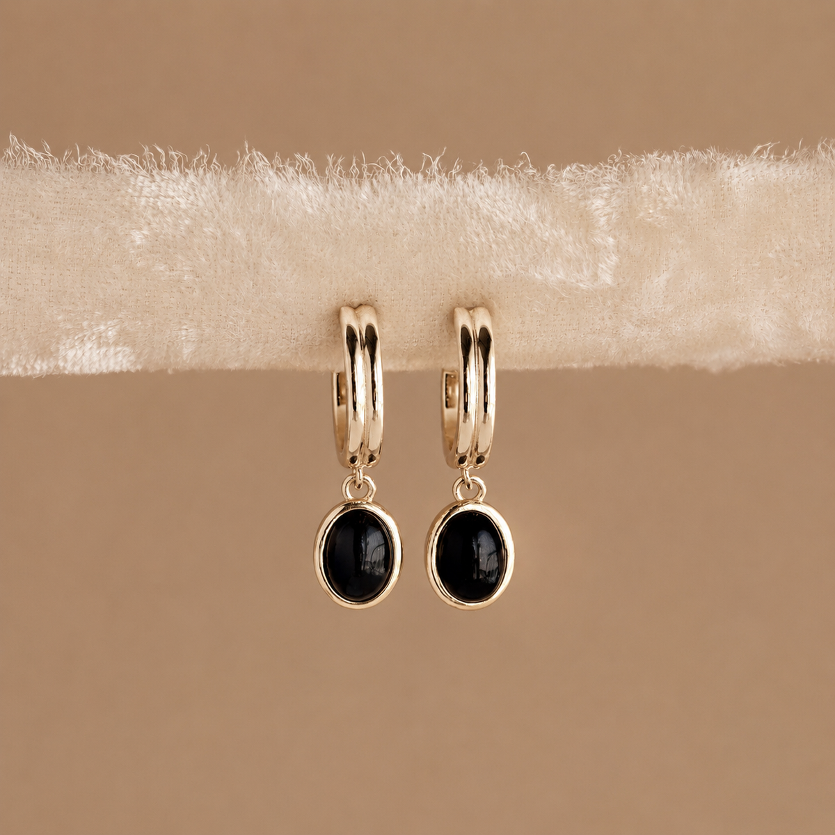 Gold hoop earrings with black stones on a beige fabric background