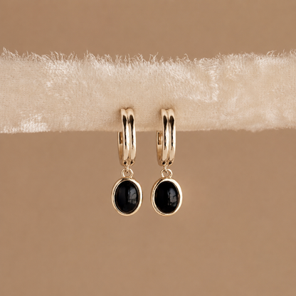 Gold hoop earrings with black stones on a beige fabric background