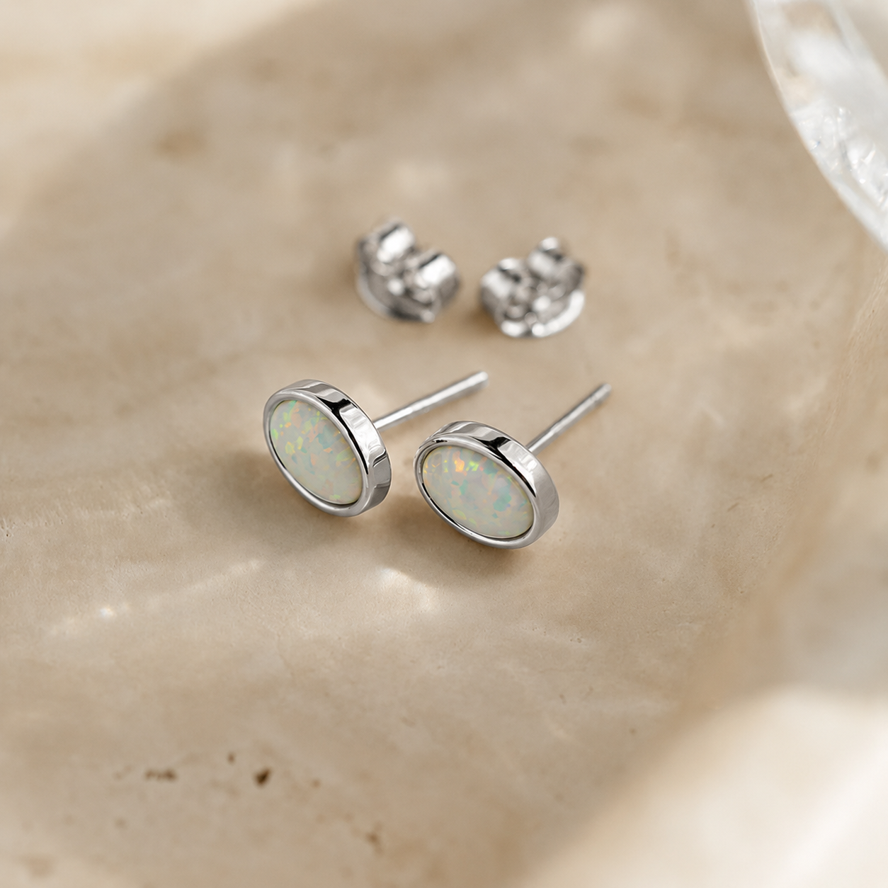 Pair of silver stud earrings with opal stones on a beige surface
