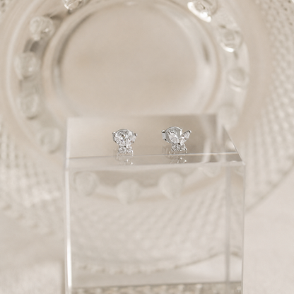 Pair of diamond stud earrings on a clear stand with a decorative white background
